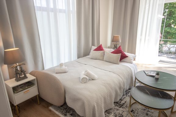 Ferienwohnung Miesbach – Liebelei: Helles Wohnzimmer mit Schlafcouch und stilvollen Details Helles Schlafzimmer mit einem Bett, eleganten Kissen und einem kleinen Tisch.