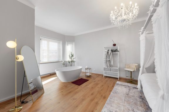 Ferienwohnung Miesbach – Liebelei: Modernes Schlafzimmer mit freistehender Badewanne Modernes Badezimmer mit freistehender Badewanne, eleganter Lampe und hellem Interieur.